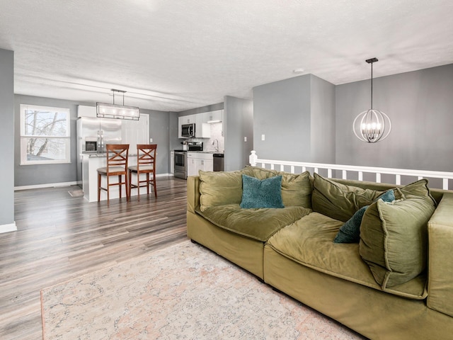 living room with baseboards, a textured ceiling, wood finished floors, and an inviting chandelier