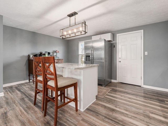 kitchen featuring stainless steel refrigerator with ice dispenser, baseboards, white cabinets, wood finished floors, and a kitchen bar