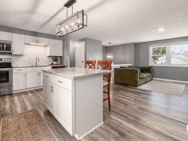 kitchen with dark wood-style floors, appliances with stainless steel finishes, a sink, a chandelier, and a kitchen breakfast bar