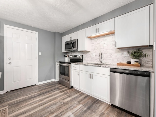 kitchen with tasteful backsplash, white cabinets, dark wood-style floors, stainless steel appliances, and a sink