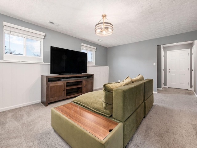 living room featuring a textured ceiling, a chandelier, light colored carpet, visible vents, and baseboards