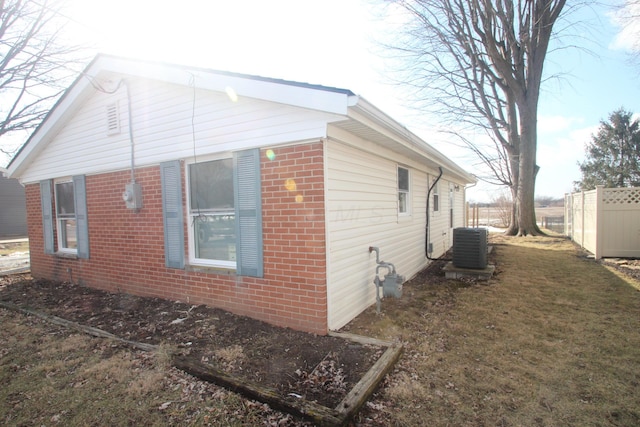 view of property exterior with brick siding, a yard, fence, and central air condition unit