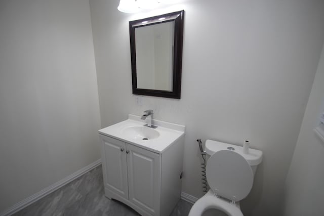 half bath with toilet, baseboards, and vanity