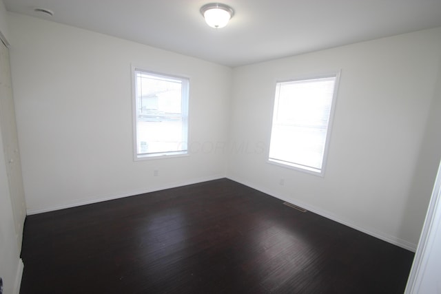 unfurnished room featuring dark wood-style floors, a wealth of natural light, visible vents, and baseboards