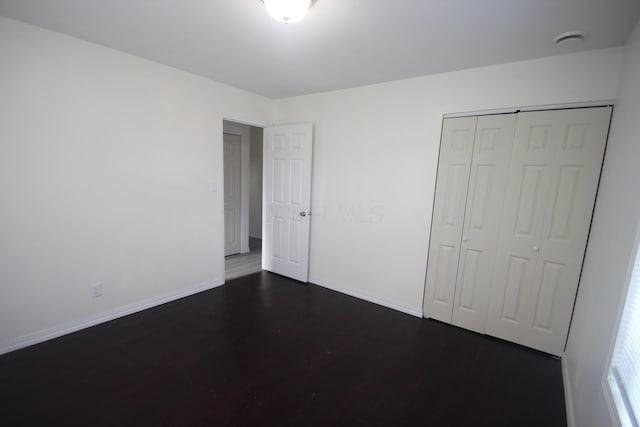 unfurnished bedroom featuring a closet, dark wood finished floors, and baseboards