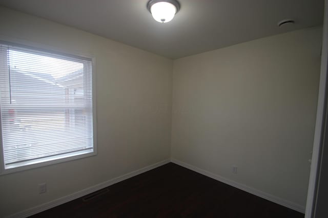 spare room with visible vents, baseboards, dark wood-style flooring, and a wealth of natural light