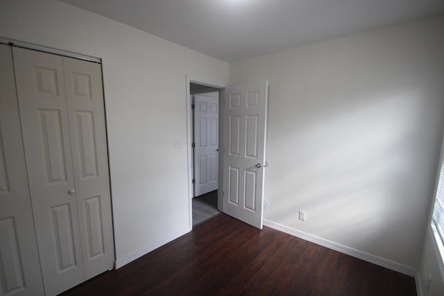 unfurnished bedroom featuring a closet, dark wood finished floors, and baseboards