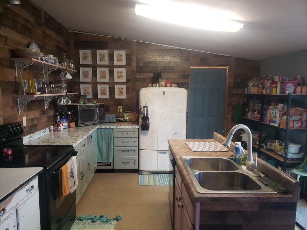 kitchen featuring black range with electric cooktop, a sink, white cabinets, light countertops, and freestanding refrigerator