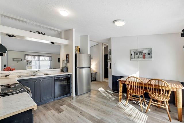 kitchen with freestanding refrigerator, a sink, light countertops, black dishwasher, and light wood-style floors