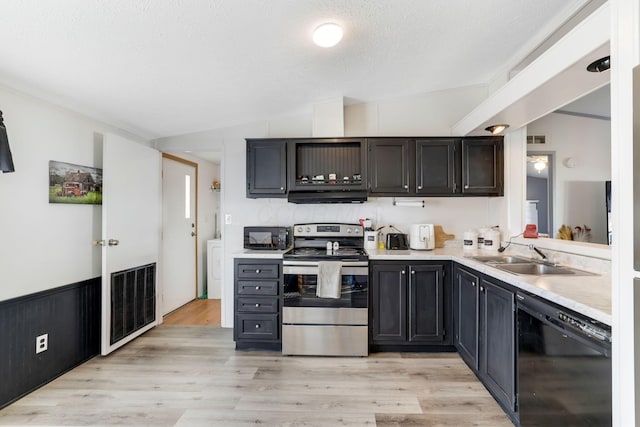 kitchen featuring black appliances, a sink, ventilation hood, light wood finished floors, and light countertops