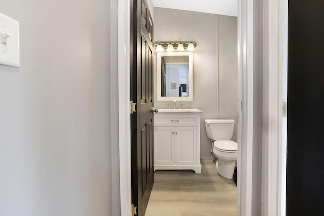 half bath with vanity, toilet, and wood finished floors