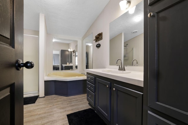 full bath featuring vanity, wood finished floors, a shower stall, a textured ceiling, and a bath