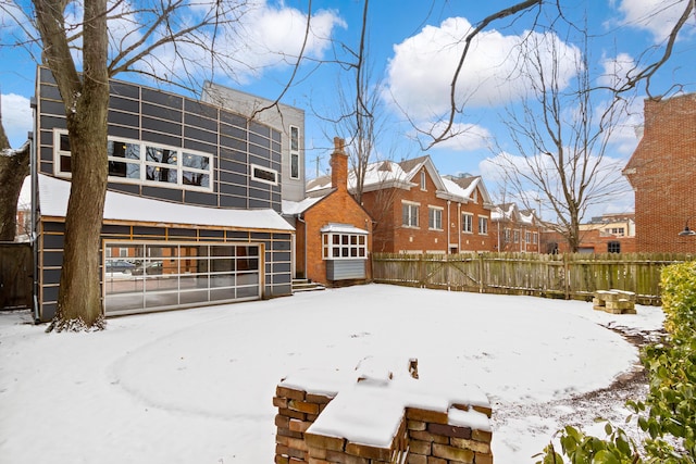 snow covered property with brick siding and fence