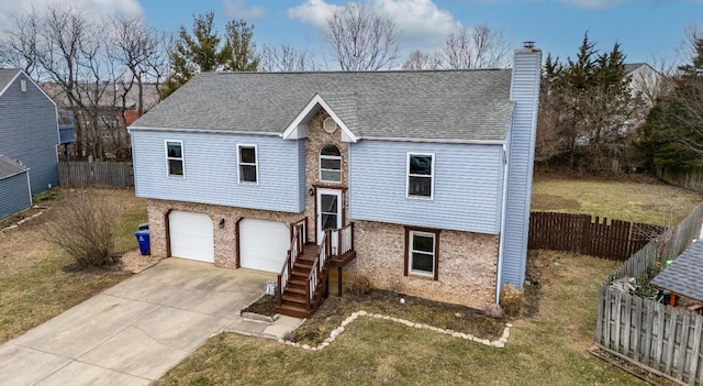 bi-level home featuring concrete driveway, a chimney, roof with shingles, fence, and brick siding