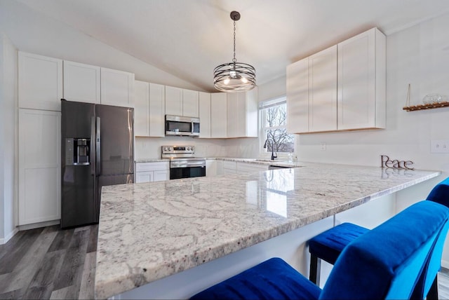 kitchen with stainless steel appliances, hanging light fixtures, white cabinetry, vaulted ceiling, and a peninsula