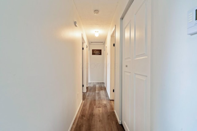 hallway with a textured ceiling, wood finished floors, and baseboards