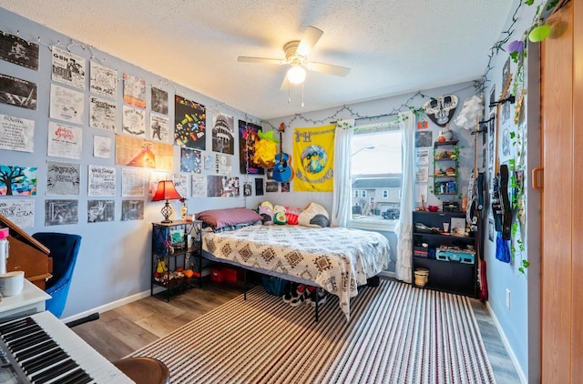 bedroom with a ceiling fan, a textured ceiling, baseboards, and wood finished floors