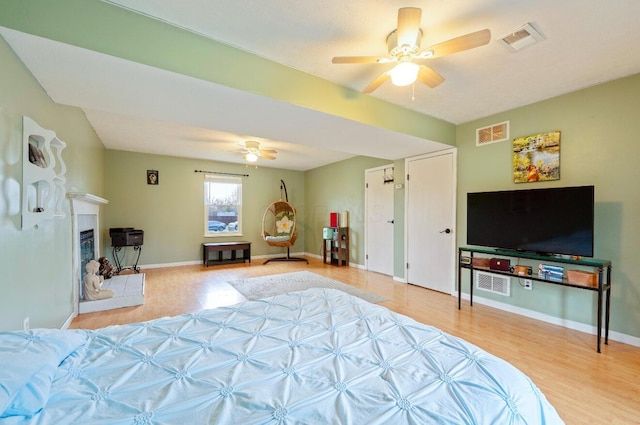 bedroom with baseboards, visible vents, a fireplace with raised hearth, and light wood finished floors