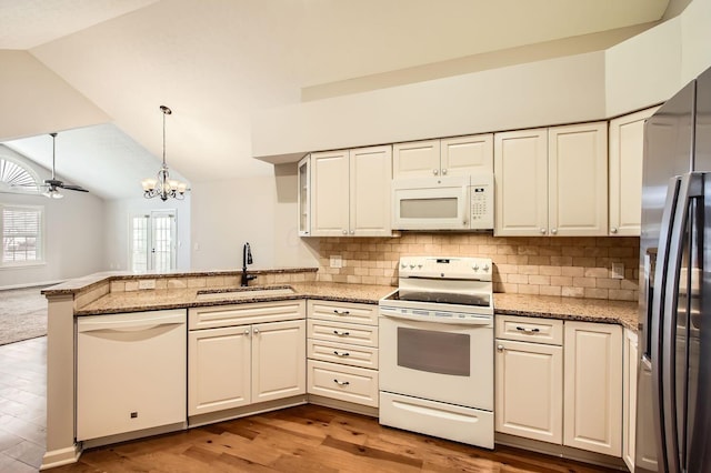 kitchen with lofted ceiling, a peninsula, white appliances, and a sink