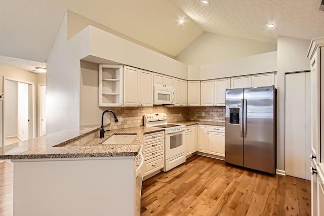 kitchen with light wood finished floors, a sink, light stone countertops, white appliances, and a peninsula