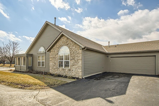 exterior space featuring stone siding, roof with shingles, an attached garage, and driveway