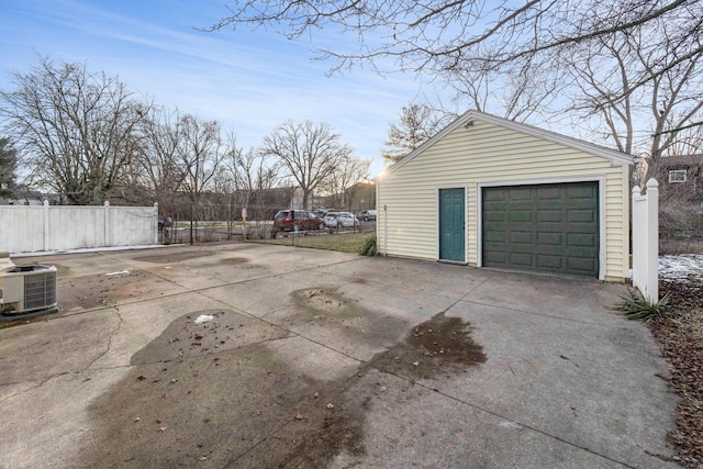 detached garage with driveway, central AC unit, and fence