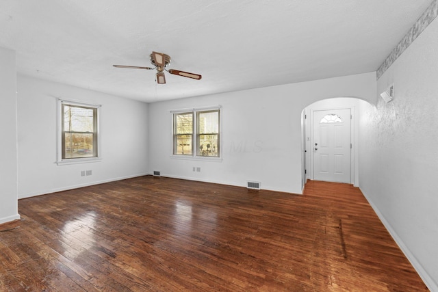 spare room featuring ceiling fan, arched walkways, dark wood finished floors, and a wealth of natural light