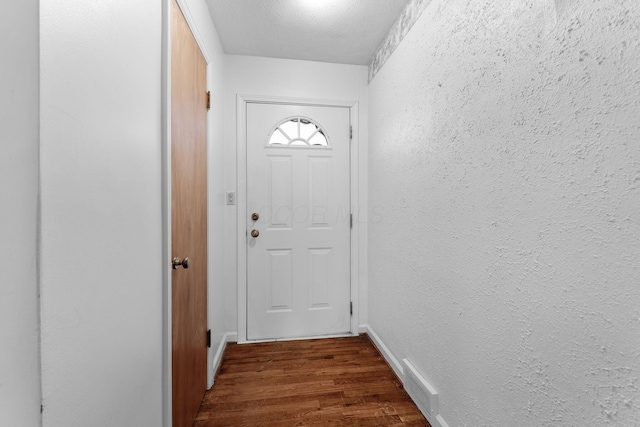 doorway featuring dark wood-style floors, visible vents, baseboards, and a textured wall