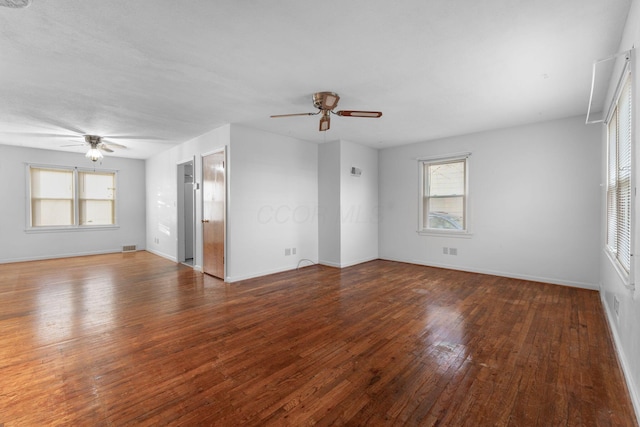 empty room featuring a ceiling fan, a wealth of natural light, dark wood finished floors, and baseboards