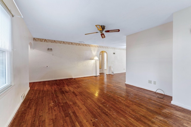 unfurnished room with a wealth of natural light, arched walkways, dark wood-style flooring, and ceiling fan