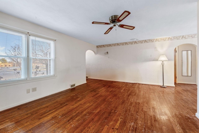 spare room featuring baseboards, visible vents, arched walkways, ceiling fan, and wood finished floors