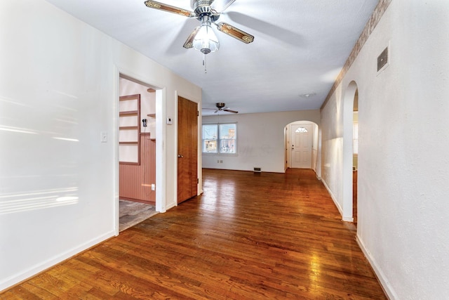 empty room featuring visible vents, arched walkways, baseboards, dark wood-style floors, and ceiling fan