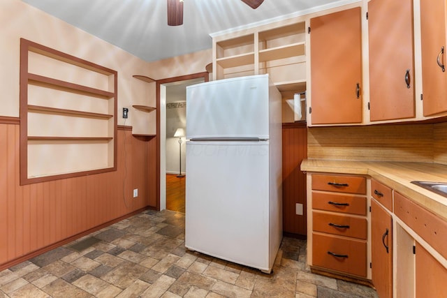 kitchen with open shelves, wainscoting, freestanding refrigerator, and stone finish flooring