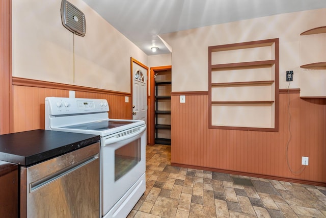 kitchen with dark countertops, electric range, stone finish floor, and wainscoting