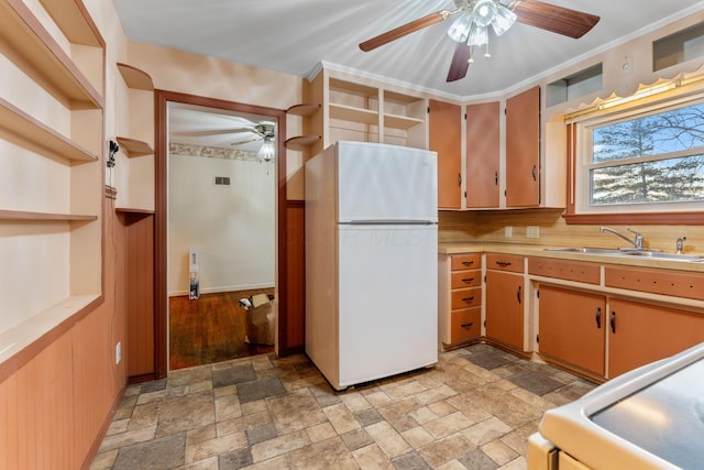 kitchen with stone finish floor, freestanding refrigerator, light countertops, open shelves, and a sink