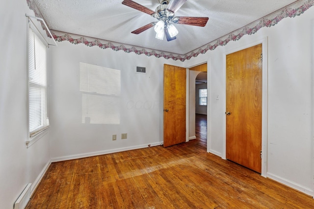 empty room with arched walkways, visible vents, a textured ceiling, wood finished floors, and baseboards