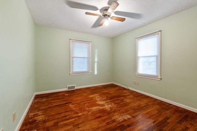 spare room featuring a textured ceiling, ceiling fan, wood finished floors, visible vents, and baseboards