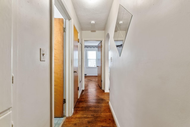 hallway with dark wood-type flooring, a textured ceiling, and baseboards