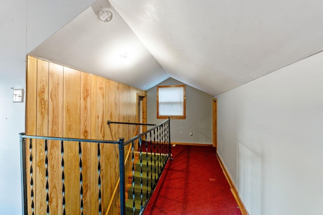 hallway featuring lofted ceiling, baseboards, dark colored carpet, and an upstairs landing