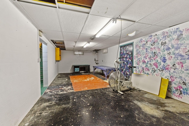 interior space with a paneled ceiling, unfinished concrete flooring, and concrete block wall