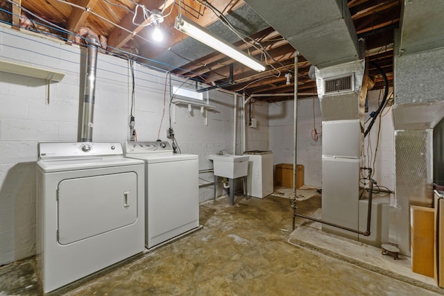 unfinished basement featuring visible vents, a sink, and washing machine and clothes dryer