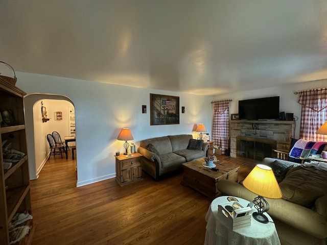 living area featuring baseboards, a fireplace, arched walkways, and wood finished floors