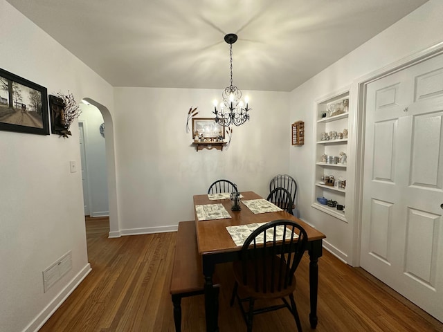 dining room featuring dark wood-style floors, arched walkways, built in shelves, visible vents, and baseboards