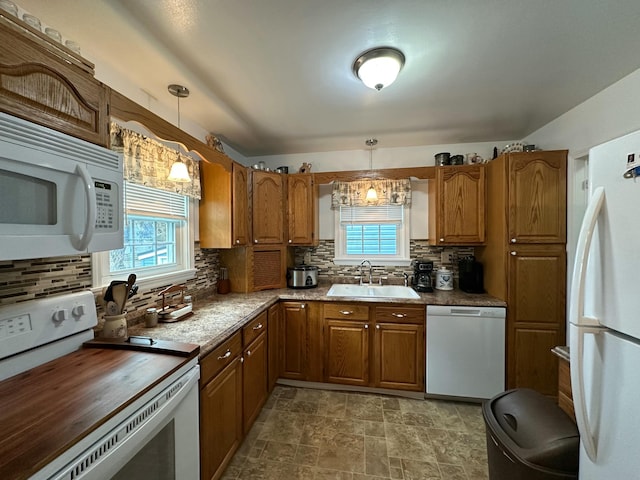 kitchen with brown cabinetry, white appliances, a sink, and backsplash