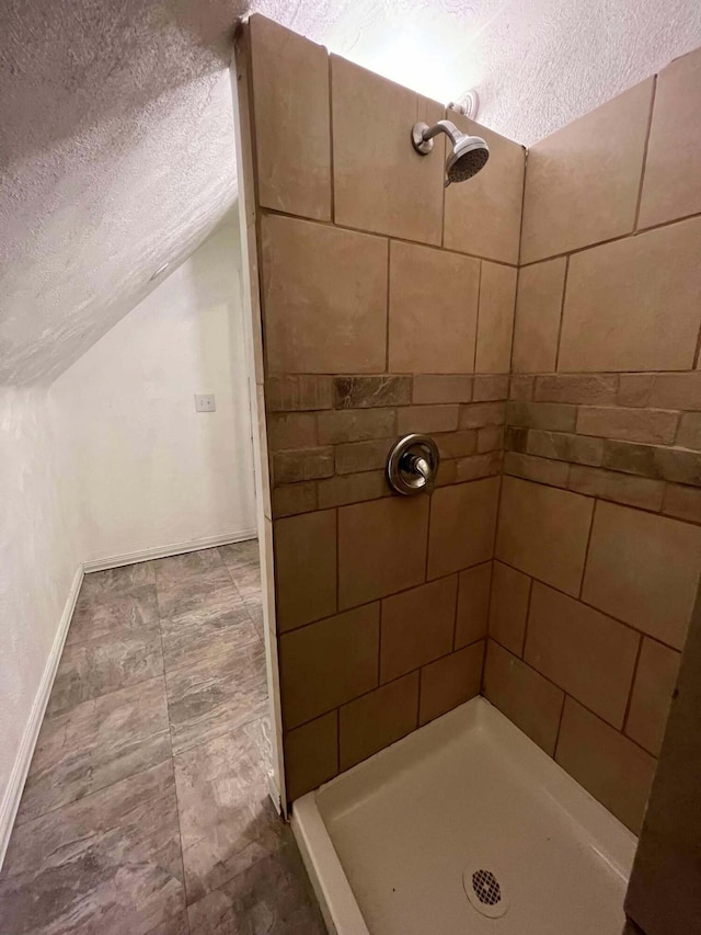 full bath featuring lofted ceiling, tiled shower, baseboards, and a textured ceiling