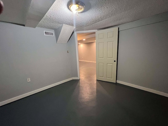 finished basement with visible vents, baseboards, and a textured ceiling