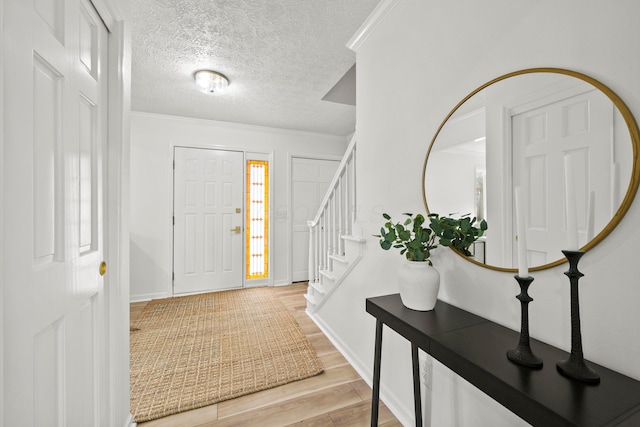 foyer featuring stairway, light wood-style floors, ornamental molding, a textured ceiling, and baseboards