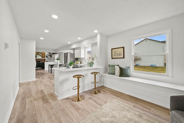 kitchen with freestanding refrigerator, a peninsula, light countertops, a kitchen bar, and white cabinetry