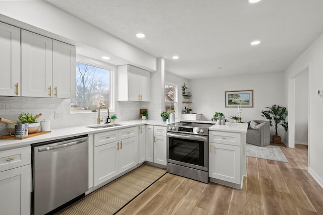 kitchen with stainless steel appliances, a peninsula, a sink, white cabinets, and light countertops