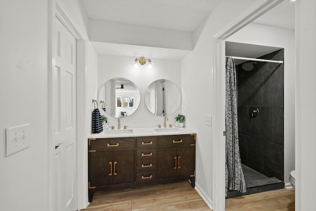 bathroom featuring double vanity, a stall shower, a sink, and wood finished floors